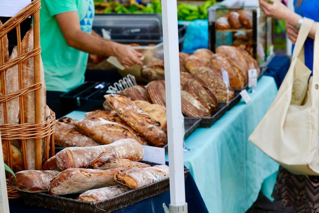 a closeup of freshly baked breads at the kelowna farmers market, with a vendor and customer exchanging bread