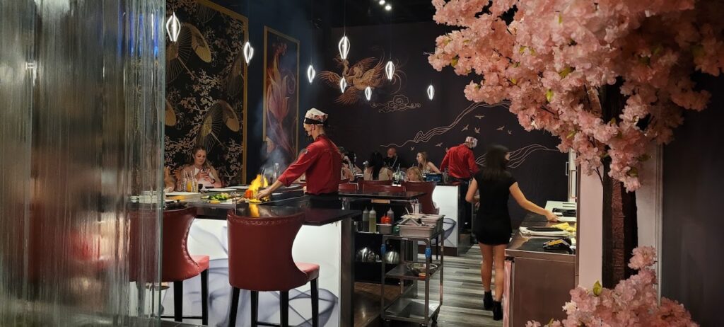 Interior view of Kasai Teppanyaki, one of Kelowna's most unique restaurants, showing their cherry blossom tree decor, and two chefs preparing meals in front of customers as part of the show experience – photo by Graham Shonfield for Google Reviews