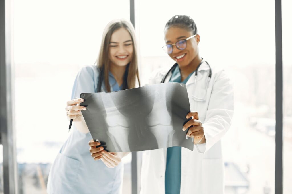 two kelowna health practitioners standing in front of a bright window, looking at two knee joints in an xray