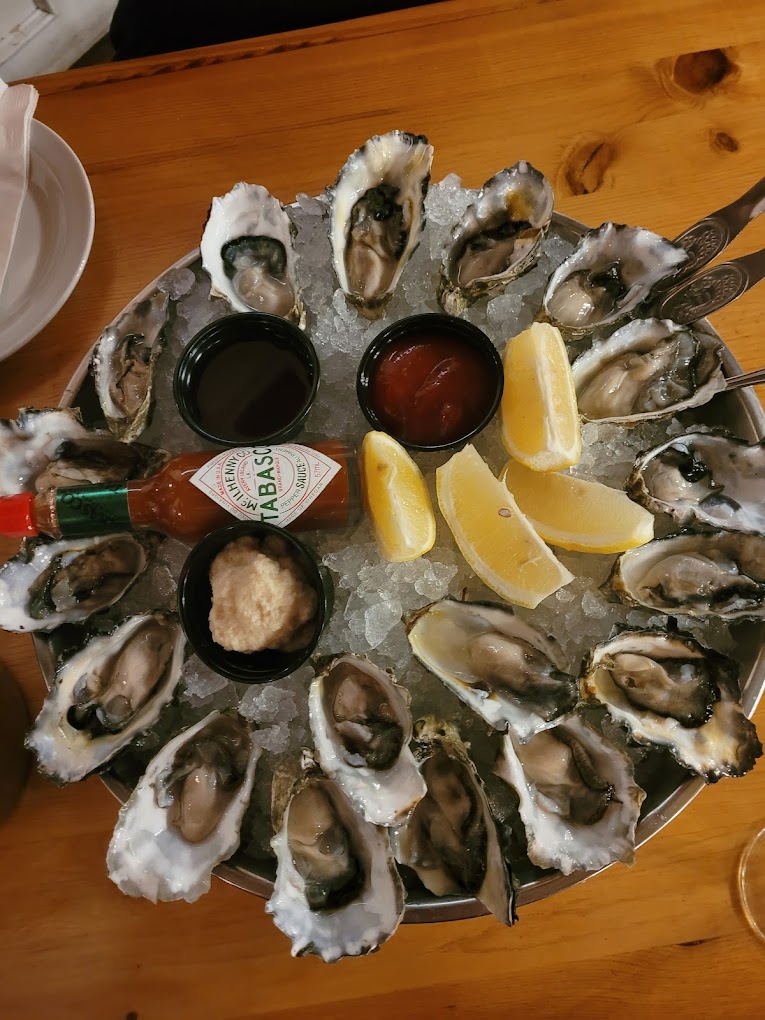 plate of oysters from West Coast Grill & Oyster Bar, with lemon wedges and a tabasco sauce bottle on a bed of ice with the oysters  – photo by JJ for Google Reviews